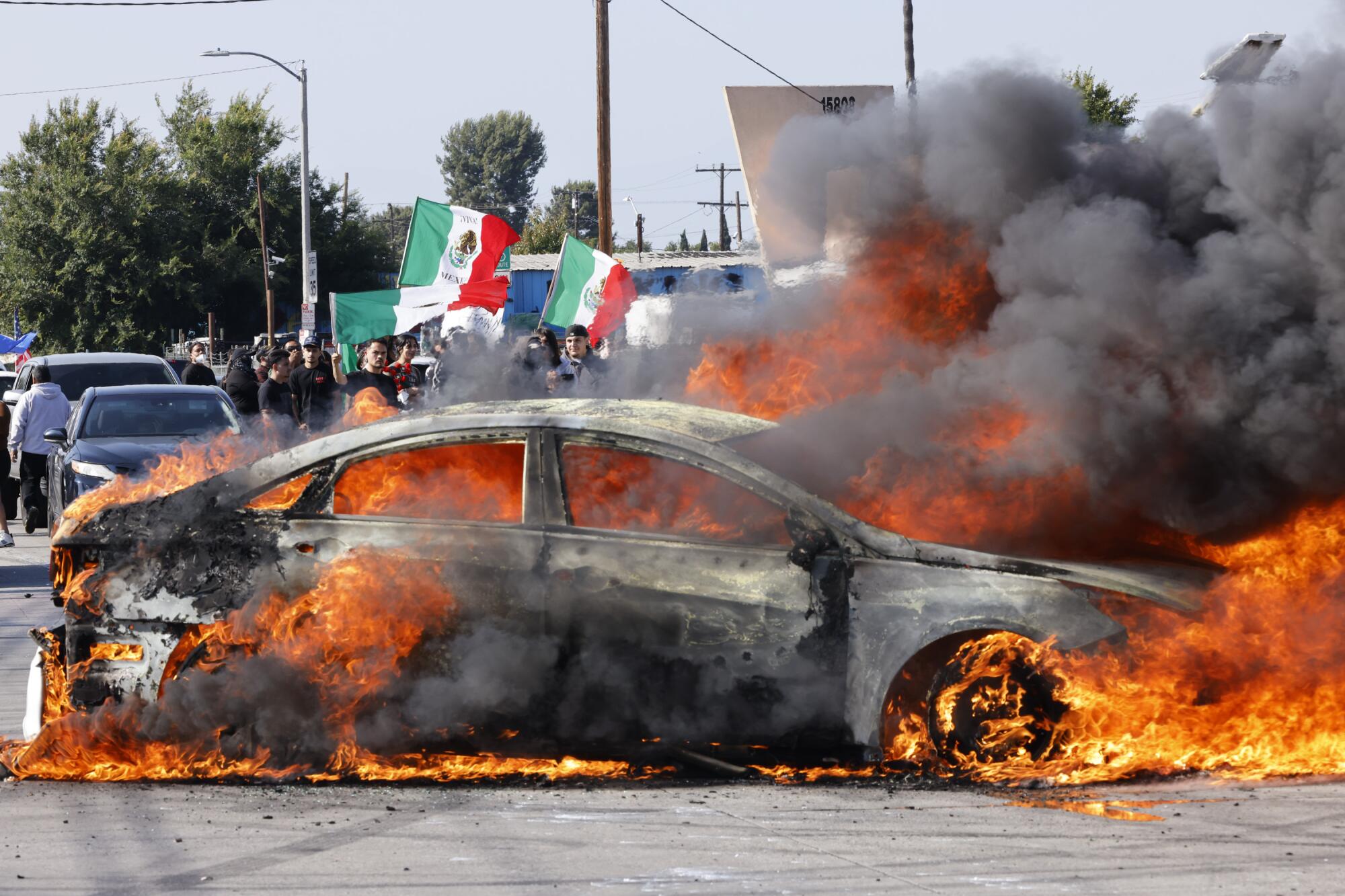 A car burns in the middle of an intersection, with green, white and red flags seen in the background