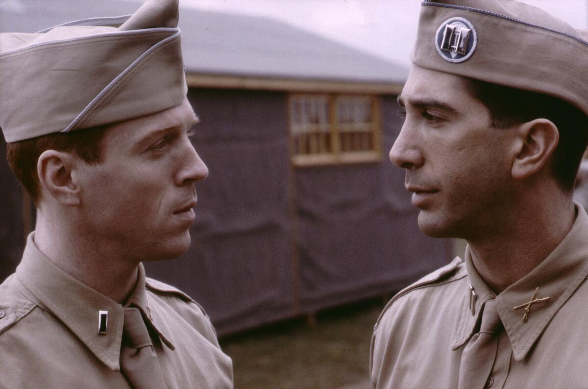 Two men in military uniform stand beside a building.