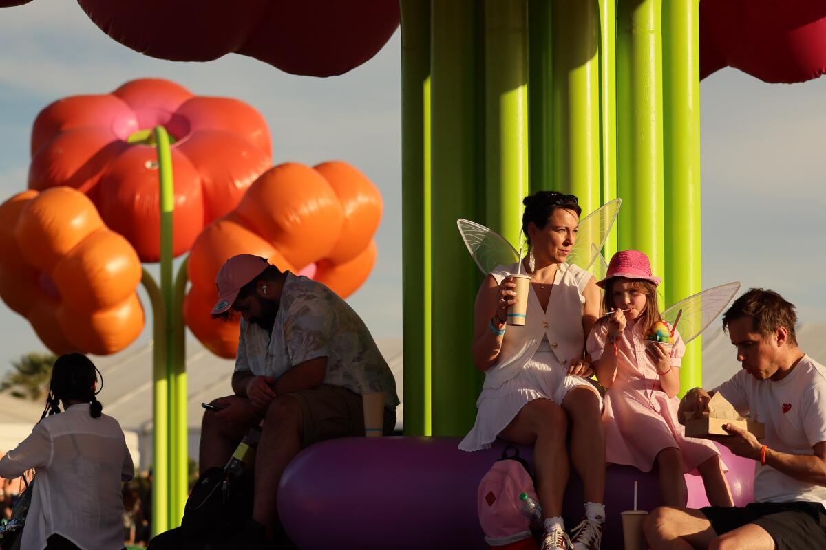 A woman and a girl wearing fairy wings and a man eat frozen ice under an art sculpture