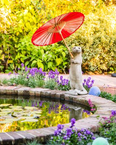 A stone otter holds a cheerful umbrella at the pond in the sun garden at Sherman Library & Gardens in Corona del Mar.