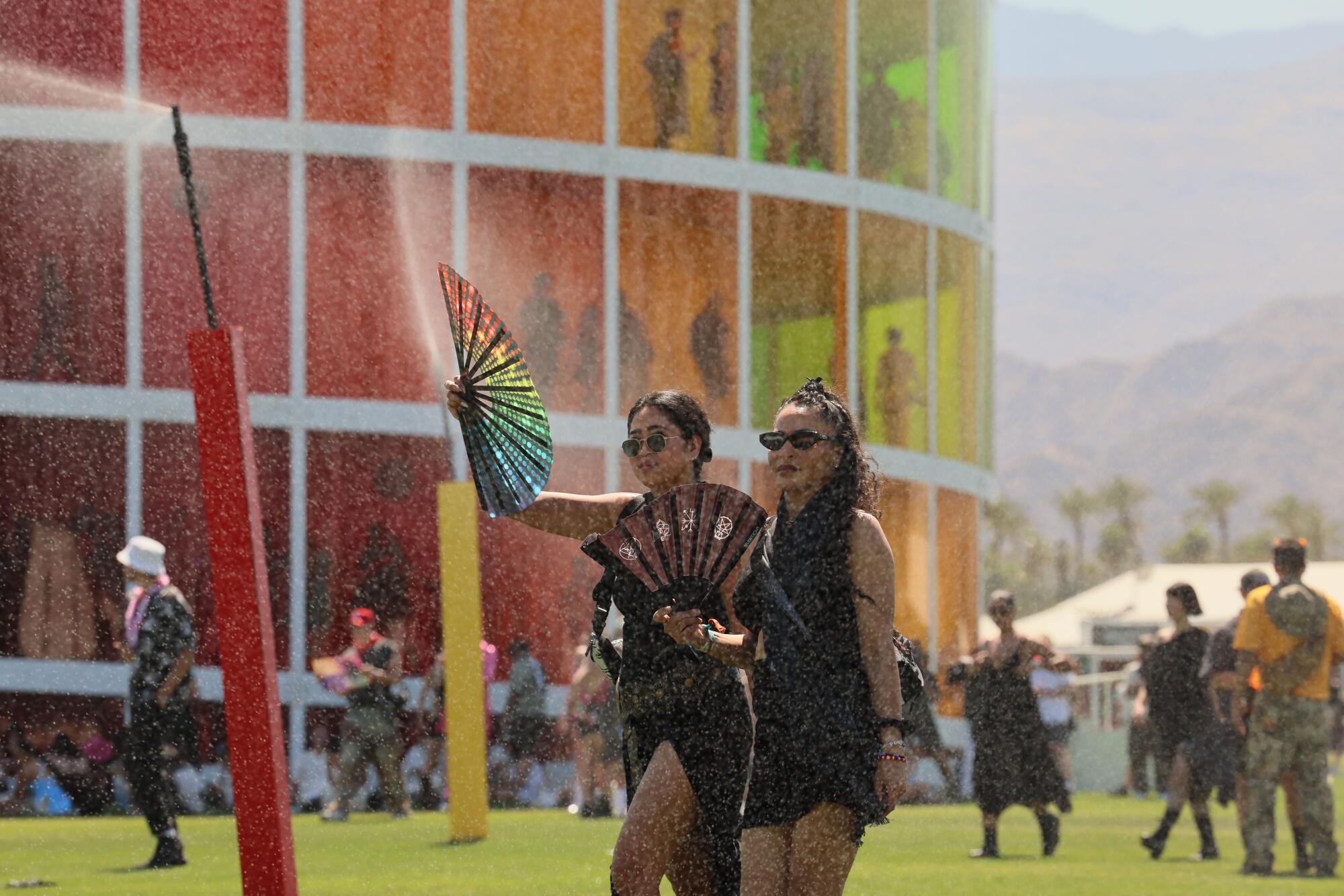 Two people with big hand fans pass a mister to keep cool.